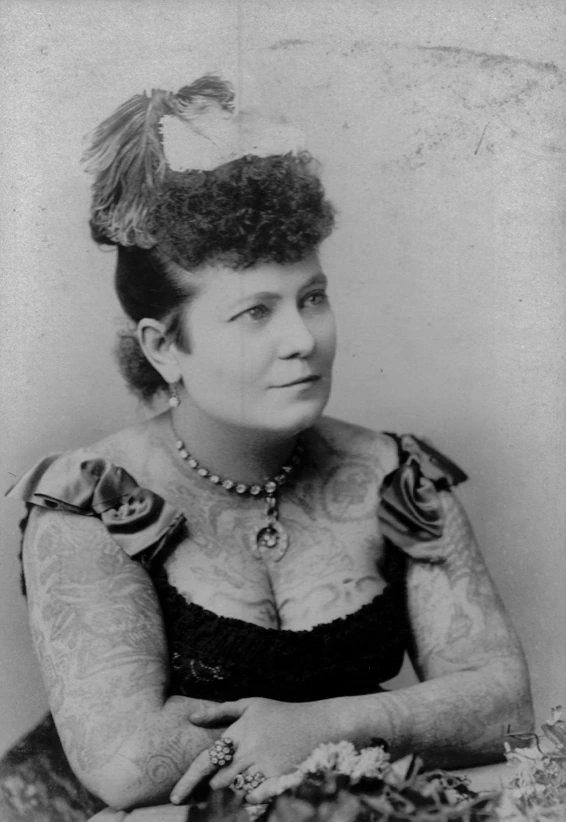 Nora Hildebrandt sentada, con un adorno en el cabello y tatuajes visibles sobre los brazos y el pecho.
