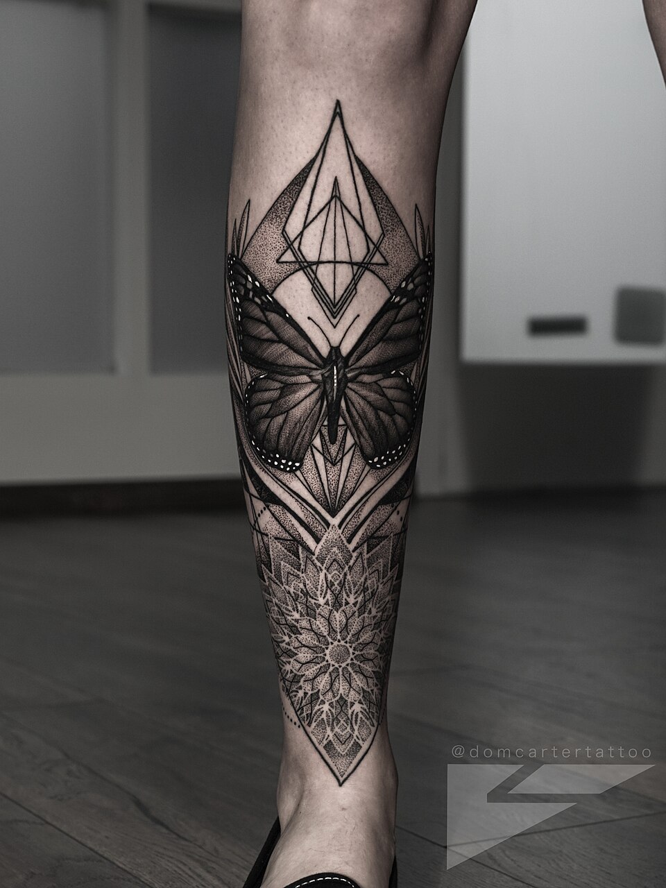 A butterfly and geometric tattoo by Dom Carter, photographed from the front.